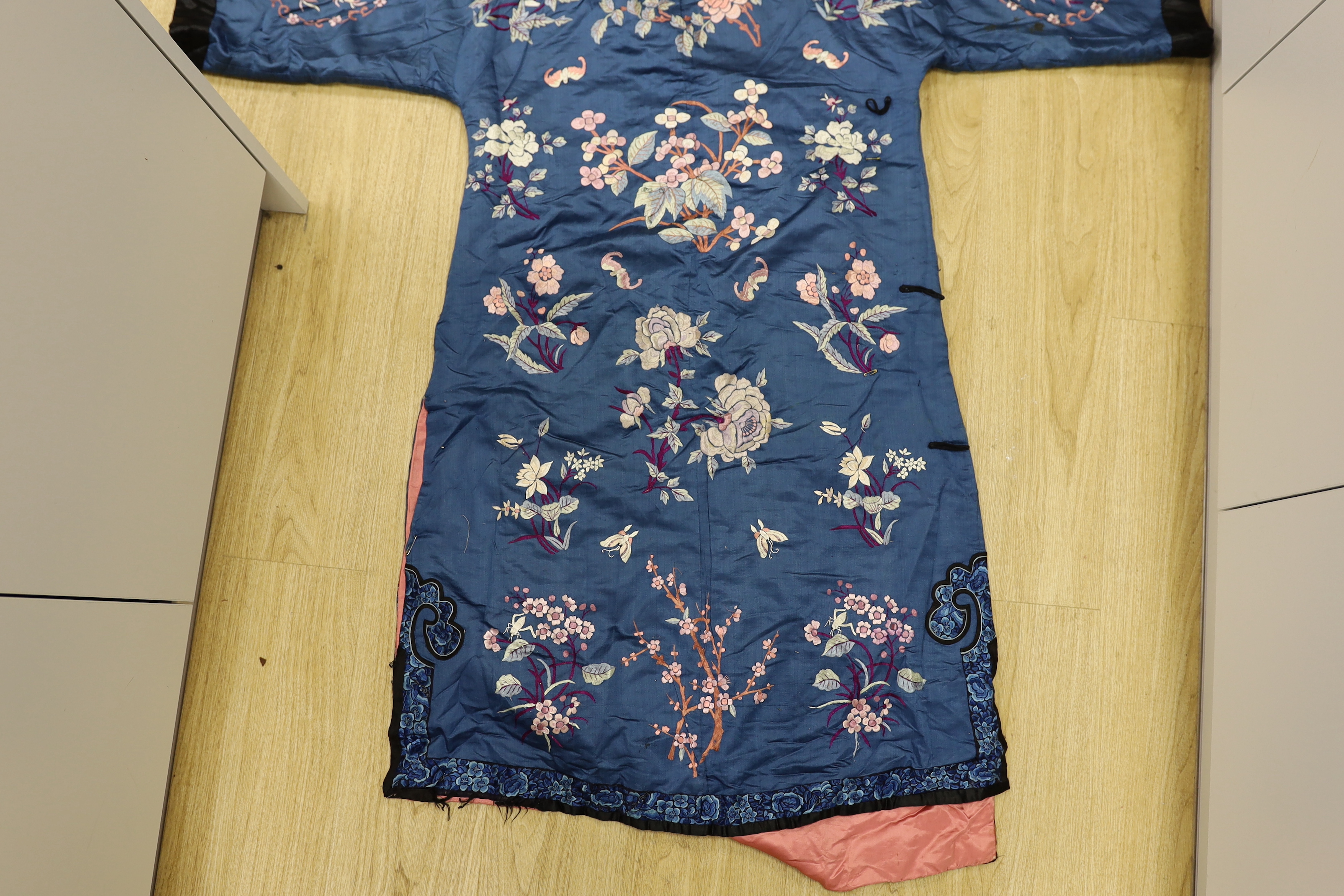 An early 20th century Chinese blue silk embroidered robe, later altered, cut and re-lined, together with various pieces of later Chinese embroidery and an earlier red silk panel with cut velvet circular motifs